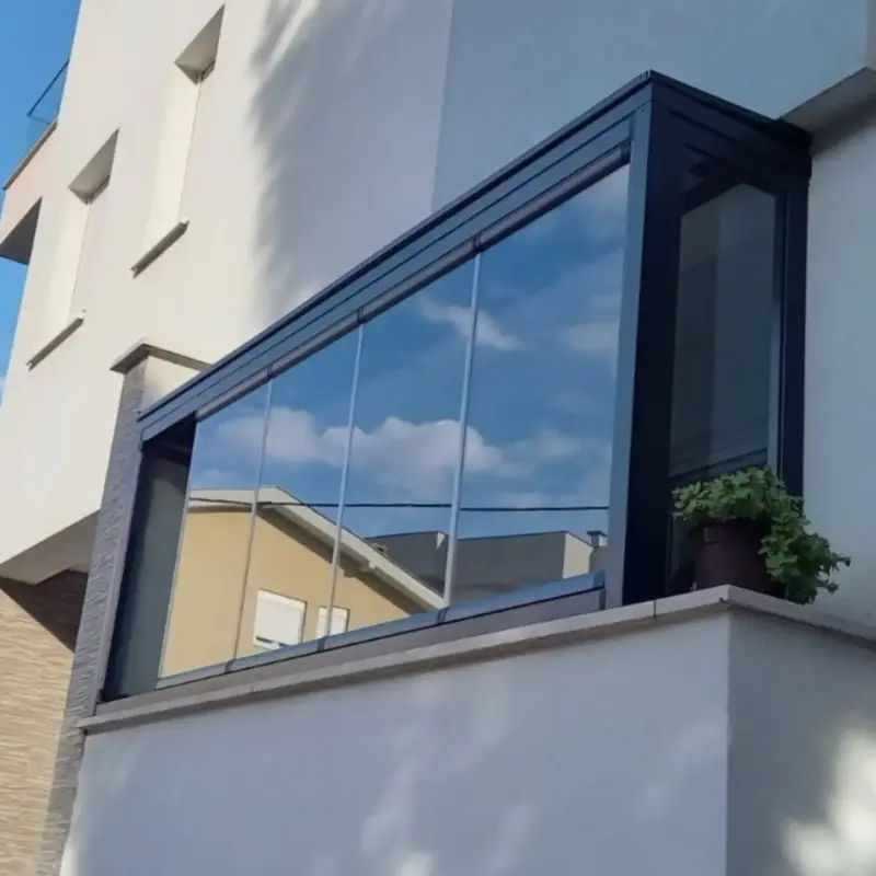 Ostakljen balkon na fasadi kuće, u staklu se ogleda nebo